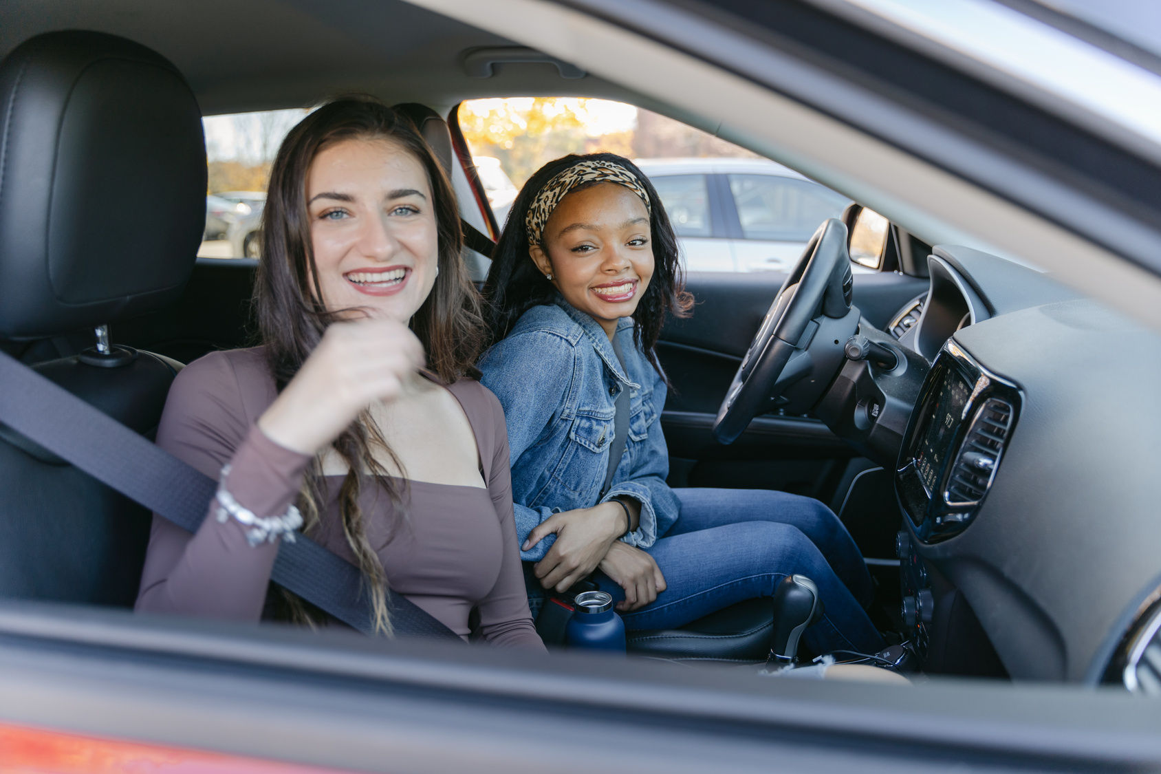 two girls sitting in a car facing a rolled down window and smiling