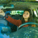 Teenage driver adjusting the rearview mirror on a sunny day
